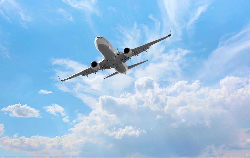 An aircraft soaring through a blue sky with white clouds.