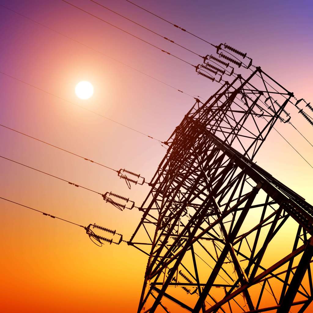 A high voltage direct current pylon is silhouetted against the sunset.