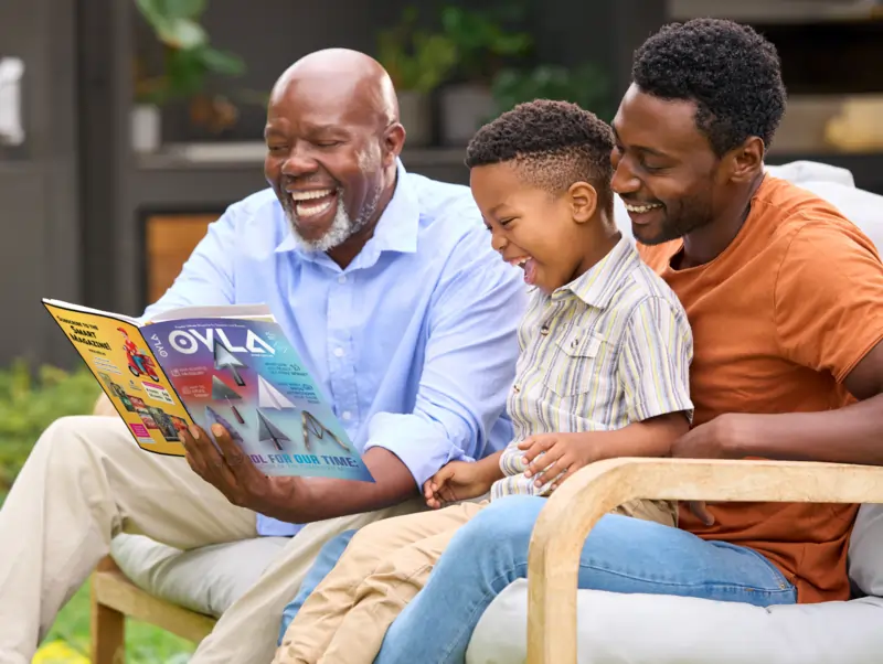 Three generations of a family sit together outdoors, smiling and reading an issue of OYLA magazine.